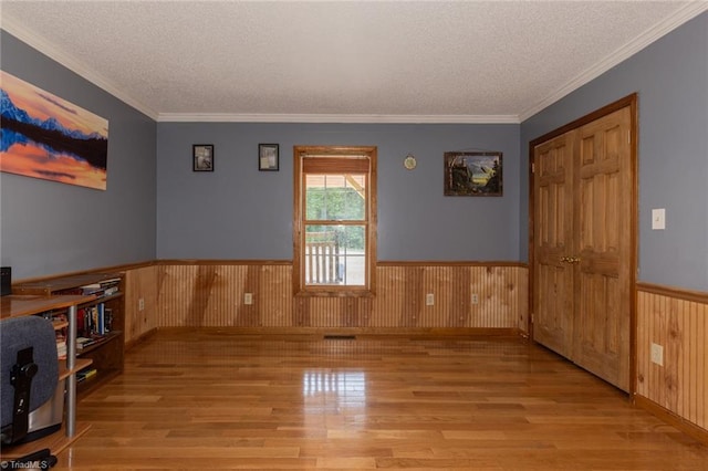 unfurnished room with light hardwood / wood-style floors, wood walls, a textured ceiling, and ornamental molding