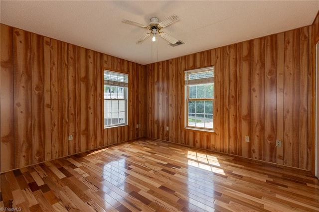 empty room with light hardwood / wood-style floors, ceiling fan, and wooden walls