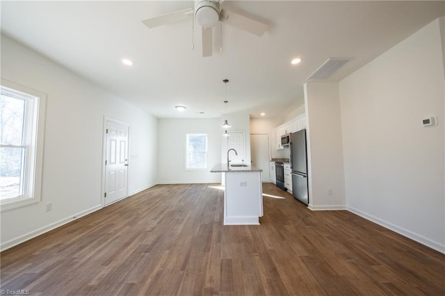 kitchen with appliances with stainless steel finishes, dark wood-type flooring, a center island with sink, white cabinetry, and hanging light fixtures