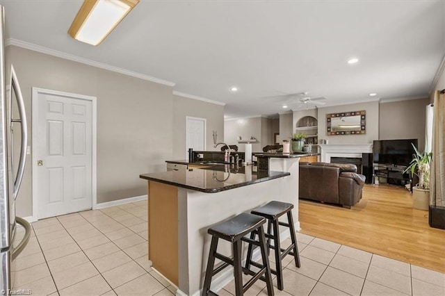 kitchen featuring ornamental molding, light tile patterned floors, an island with sink, stainless steel fridge, and a breakfast bar