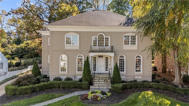 view of front of home with a shingled roof, a balcony, and stucco siding