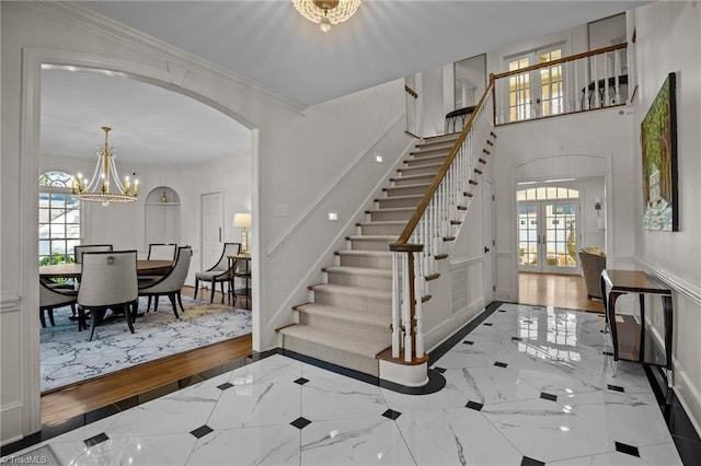 foyer featuring an inviting chandelier, stairs, baseboards, ornamental molding, and arched walkways