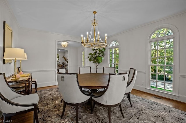 dining room featuring a notable chandelier, visible vents, ornamental molding, arched walkways, and wood finished floors