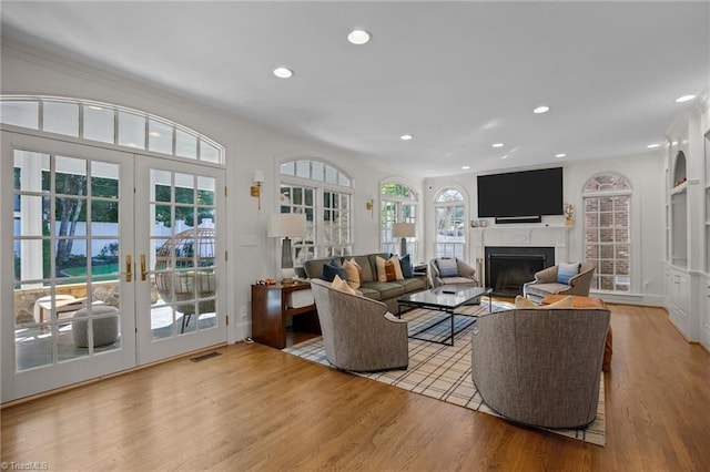 living area featuring recessed lighting, wood finished floors, a fireplace, french doors, and crown molding