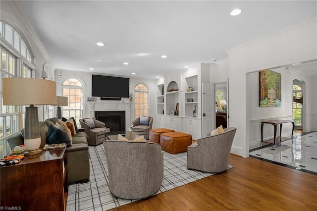 living room featuring ornamental molding, built in features, wood finished floors, and a fireplace