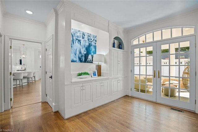 doorway featuring an inviting chandelier, light wood-style flooring, visible vents, french doors, and crown molding