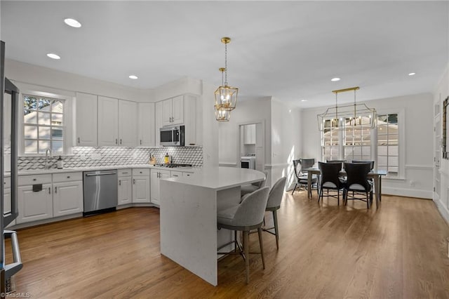 kitchen featuring tasteful backsplash, white cabinets, appliances with stainless steel finishes, light countertops, and wood finished floors
