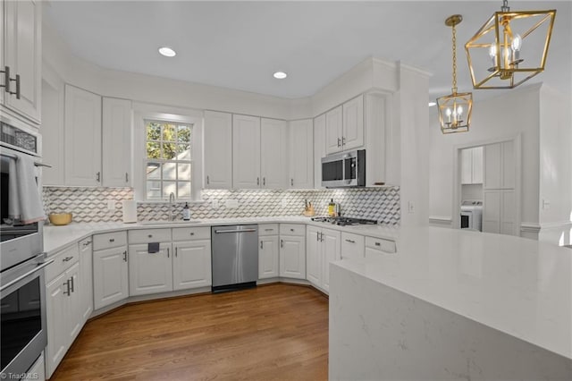 kitchen featuring an inviting chandelier, appliances with stainless steel finishes, a sink, white cabinetry, and washer / clothes dryer
