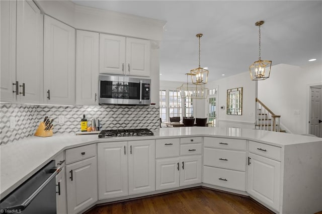 kitchen with a chandelier, appliances with stainless steel finishes, light countertops, white cabinets, and backsplash