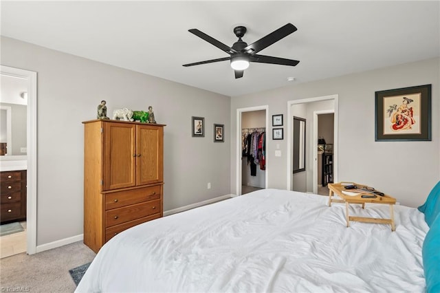 bedroom featuring light carpet, ensuite bathroom, a walk in closet, baseboards, and ceiling fan
