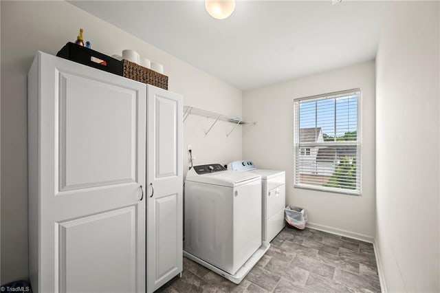 washroom with washer and clothes dryer, baseboards, stone finish floors, and cabinet space