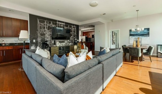 living area with an inviting chandelier, wood finished floors, and visible vents