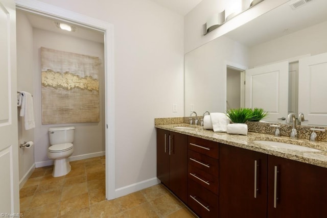 bathroom with double vanity, toilet, baseboards, and a sink