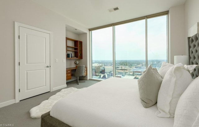 bedroom with visible vents, baseboards, carpet, a wall of windows, and built in study area