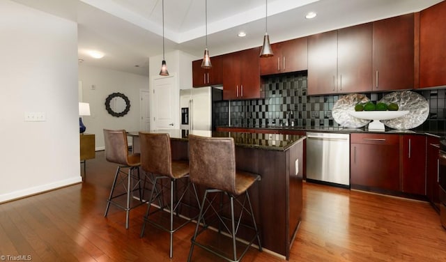 kitchen featuring dark wood finished floors, decorative backsplash, a center island, and stainless steel appliances