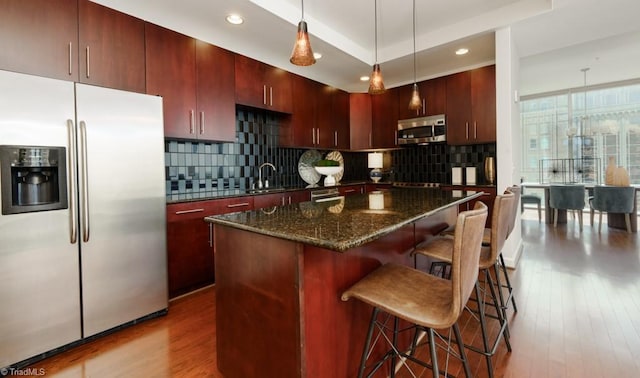 kitchen with a sink, decorative backsplash, appliances with stainless steel finishes, and wood finished floors