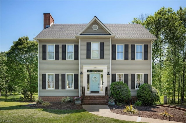 colonial inspired home featuring fence, a chimney, and a front yard