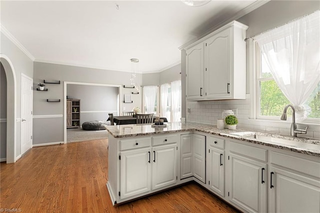 kitchen with a peninsula, arched walkways, white cabinets, tasteful backsplash, and a sink