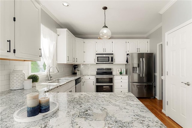 kitchen featuring crown molding, appliances with stainless steel finishes, light stone countertops, a sink, and white cabinetry