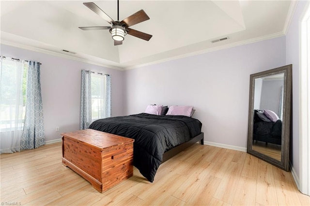 bedroom with baseboards, a tray ceiling, light wood finished floors, and visible vents