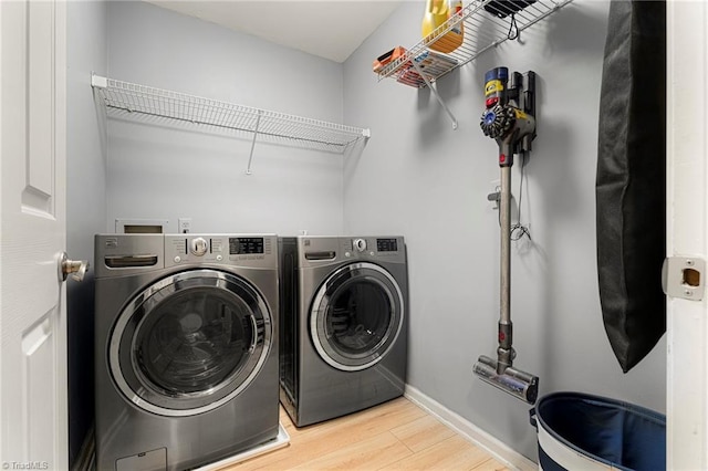 washroom with laundry area, washer and clothes dryer, light wood finished floors, and baseboards