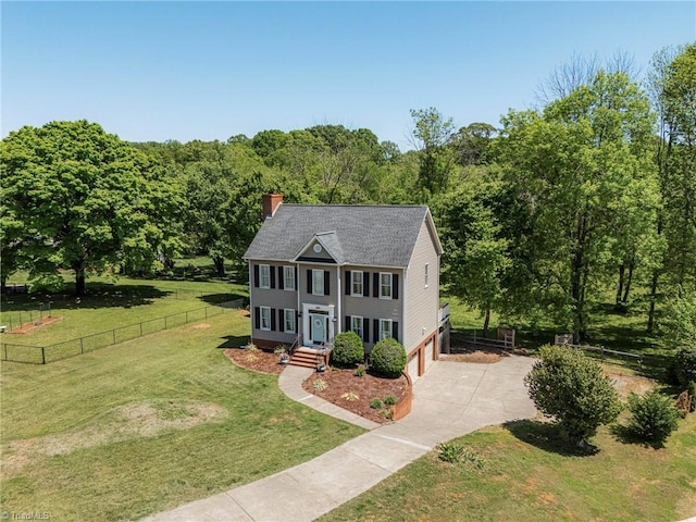 colonial-style house featuring driveway, a chimney, fence, a front lawn, and an attached garage