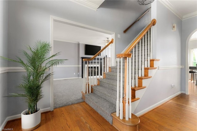 stairway with arched walkways, baseboards, ornamental molding, and wood finished floors