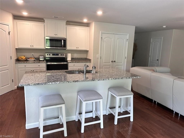 kitchen featuring sink, a breakfast bar area, appliances with stainless steel finishes, white cabinets, and a center island with sink