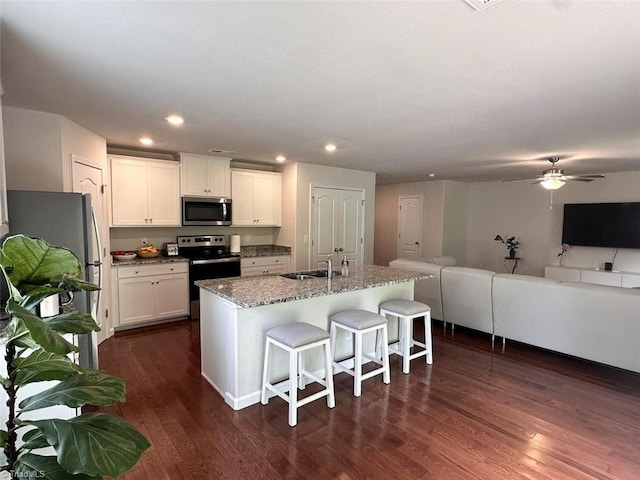 kitchen with stainless steel appliances, a center island with sink, white cabinets, and a kitchen bar