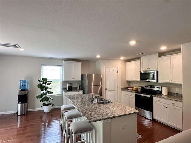 kitchen with white cabinetry, sink, stainless steel appliances, and an island with sink