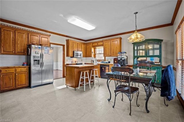 kitchen with a kitchen breakfast bar, appliances with stainless steel finishes, pendant lighting, a kitchen island, and ornamental molding