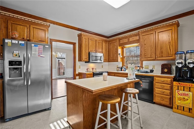 kitchen with appliances with stainless steel finishes, ornamental molding, a breakfast bar, an inviting chandelier, and a kitchen island