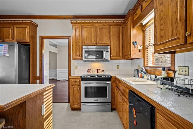 kitchen featuring tile counters, sink, stainless steel appliances, crown molding, and decorative backsplash