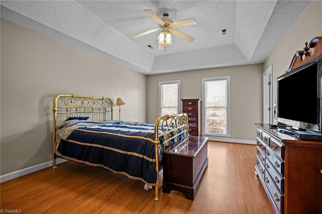 bedroom with ceiling fan, a raised ceiling, a textured ceiling, and light hardwood / wood-style flooring