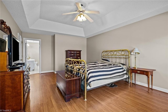 bedroom with ensuite bathroom, a textured ceiling, a tray ceiling, ceiling fan, and hardwood / wood-style floors