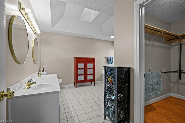 bathroom featuring vanity, a raised ceiling, a skylight, tile patterned flooring, and a textured ceiling