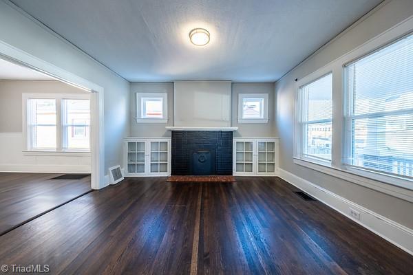 unfurnished living room with a brick fireplace, plenty of natural light, and dark wood-type flooring