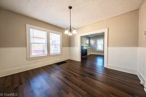 unfurnished dining area featuring dark hardwood / wood-style flooring, an inviting chandelier, and a textured ceiling