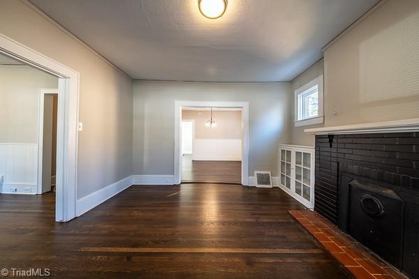 unfurnished living room featuring a brick fireplace and dark wood-type flooring