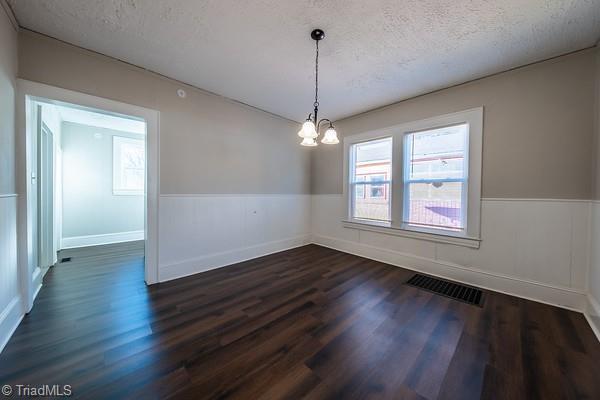 unfurnished dining area with dark wood-type flooring, a textured ceiling, plenty of natural light, and a chandelier