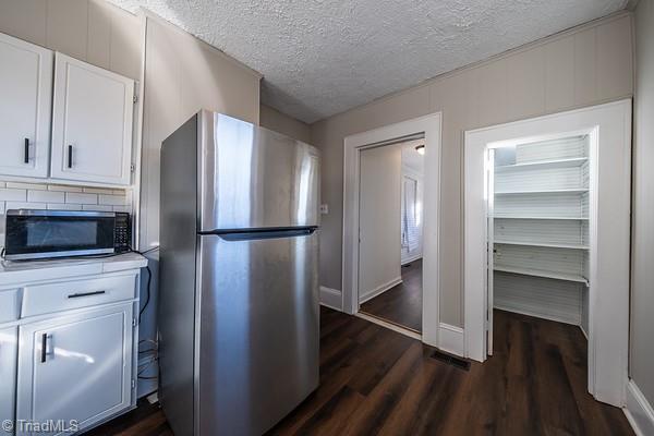 kitchen featuring a textured ceiling, appliances with stainless steel finishes, white cabinetry, and dark hardwood / wood-style floors