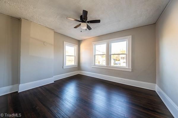 empty room featuring ceiling fan, dark wood-type flooring, and a textured ceiling