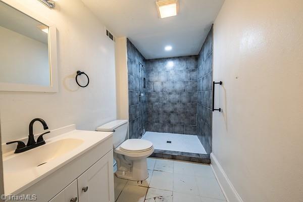 bathroom featuring toilet, vanity, and a tile shower