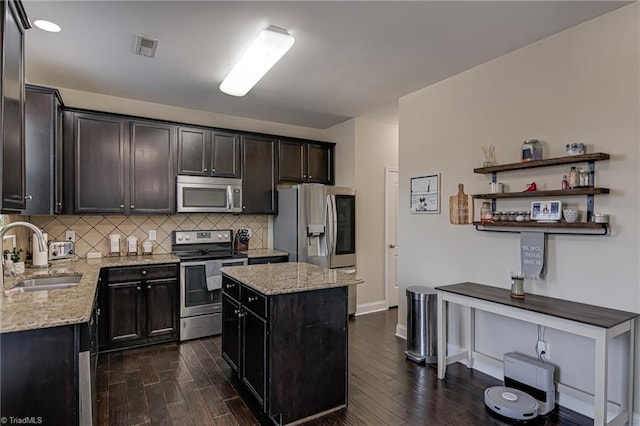 kitchen with stainless steel appliances, a center island, light stone countertops, and sink