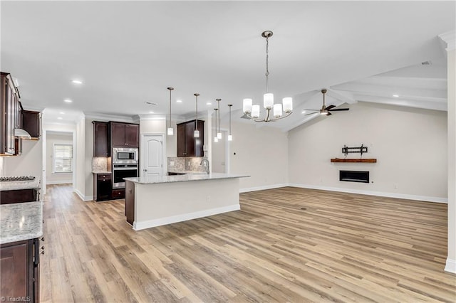 kitchen featuring stainless steel appliances, dark brown cabinets, light stone countertops, pendant lighting, and ceiling fan with notable chandelier