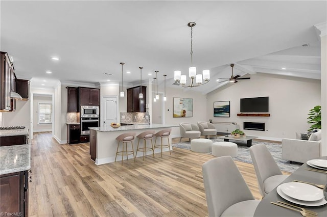 interior space featuring light wood-type flooring, ornamental molding, ceiling fan with notable chandelier, and lofted ceiling with beams