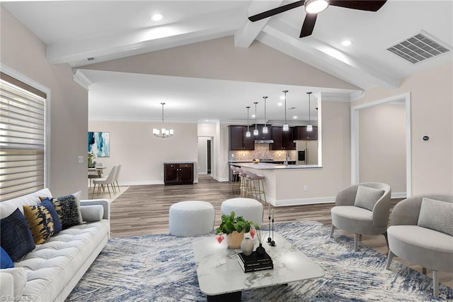 living room featuring ceiling fan with notable chandelier, dark wood-type flooring, and vaulted ceiling with beams