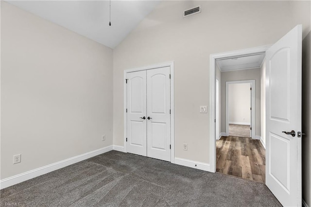 unfurnished bedroom featuring vaulted ceiling, a closet, and dark colored carpet