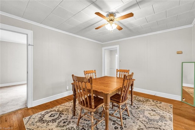 dining area with ornamental molding, light wood-type flooring, ceiling fan, and wooden walls