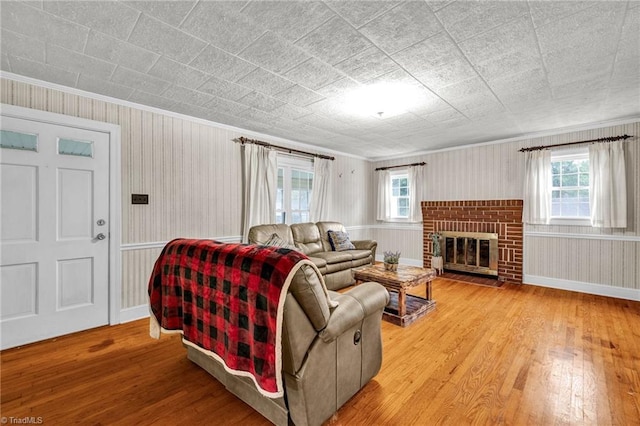 living room with wood walls, light hardwood / wood-style flooring, a fireplace, and ornamental molding